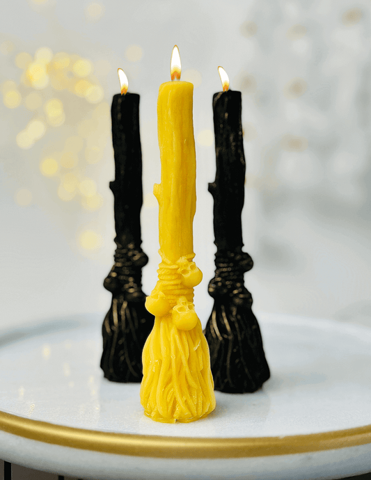 Witchcraft-inspired candles on a tray, featuring a yellow broom candle and black skull candles, ideal for Halloween.