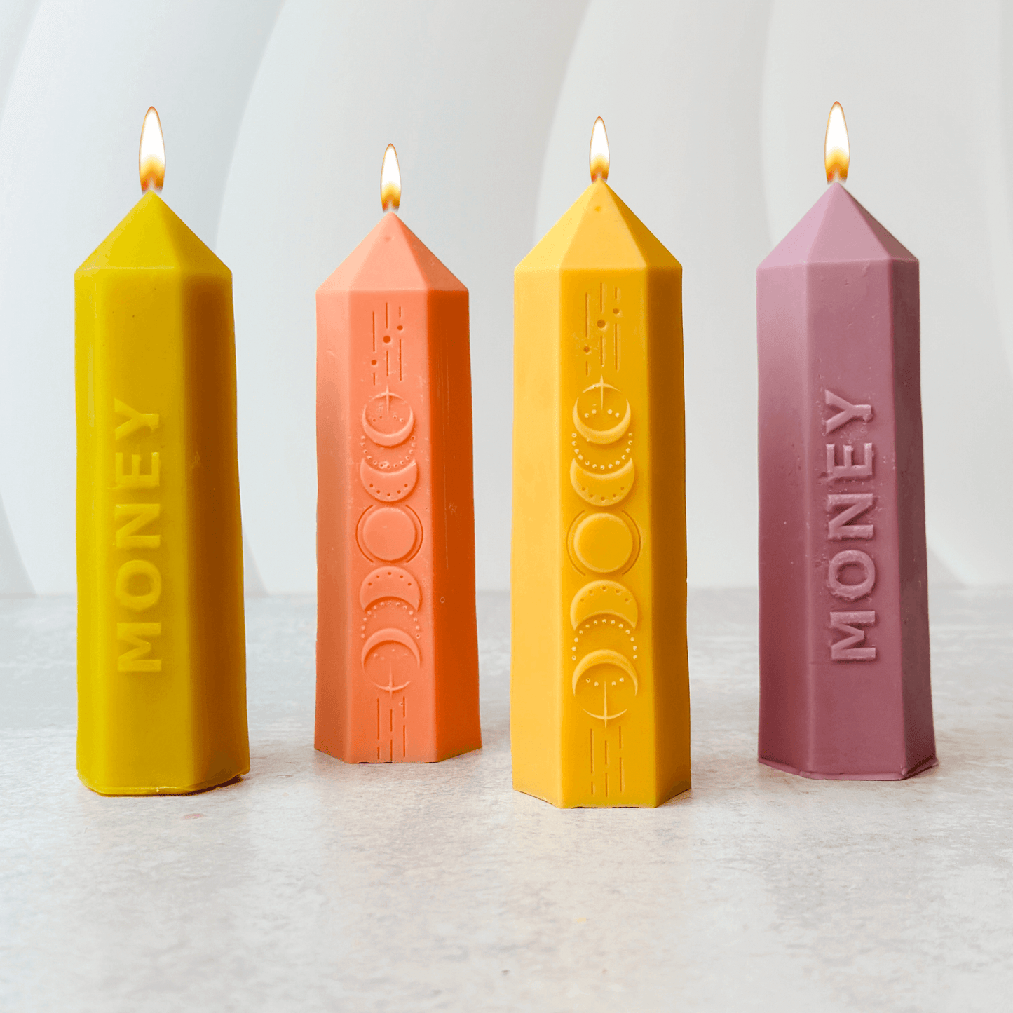 Four colorful candles in various shapes and sizes, labeled for money attraction, inspired by moon phases.