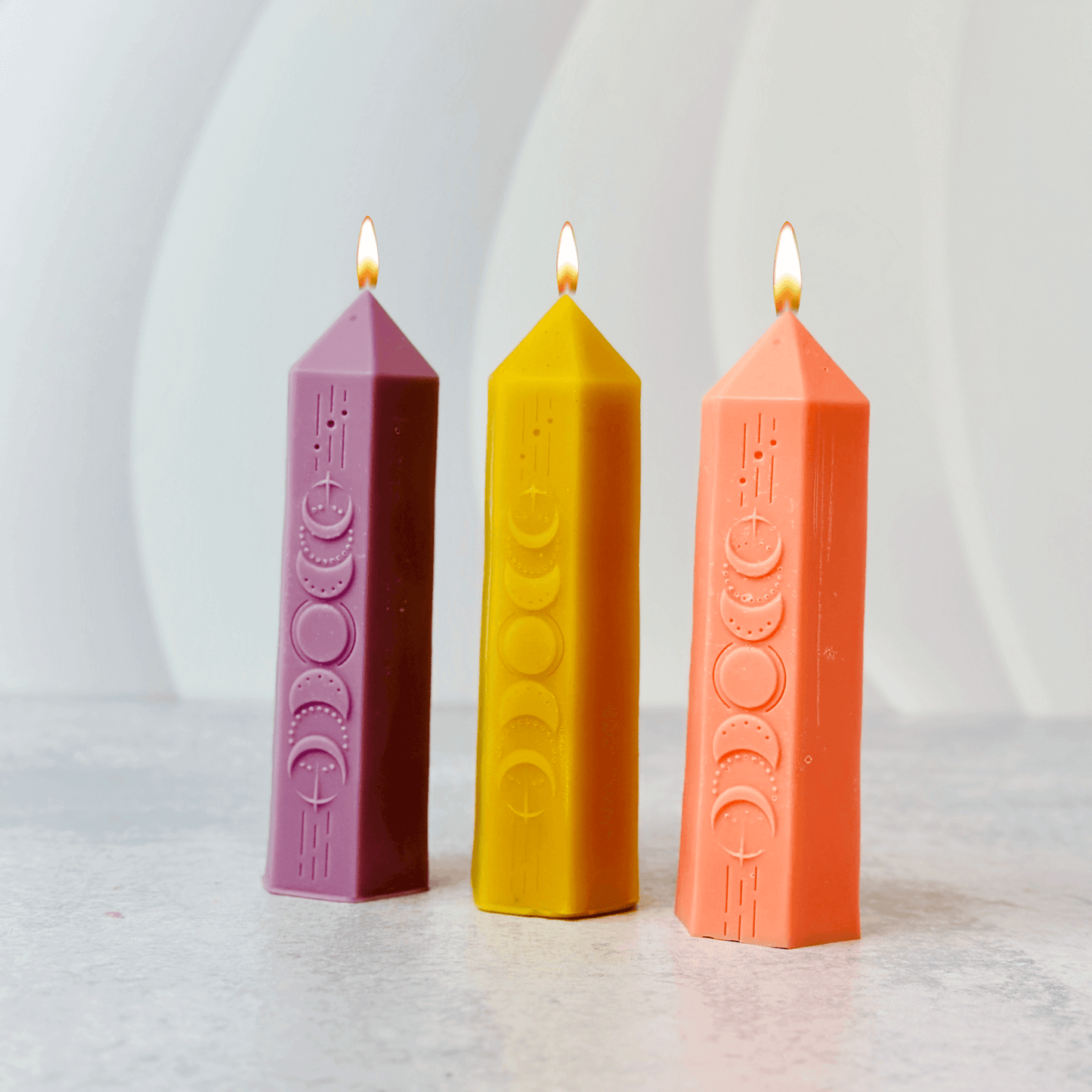 Three colorful pillar candles in purple, yellow, and orange, featuring moon phase designs, ideal for witchcraft rituals.