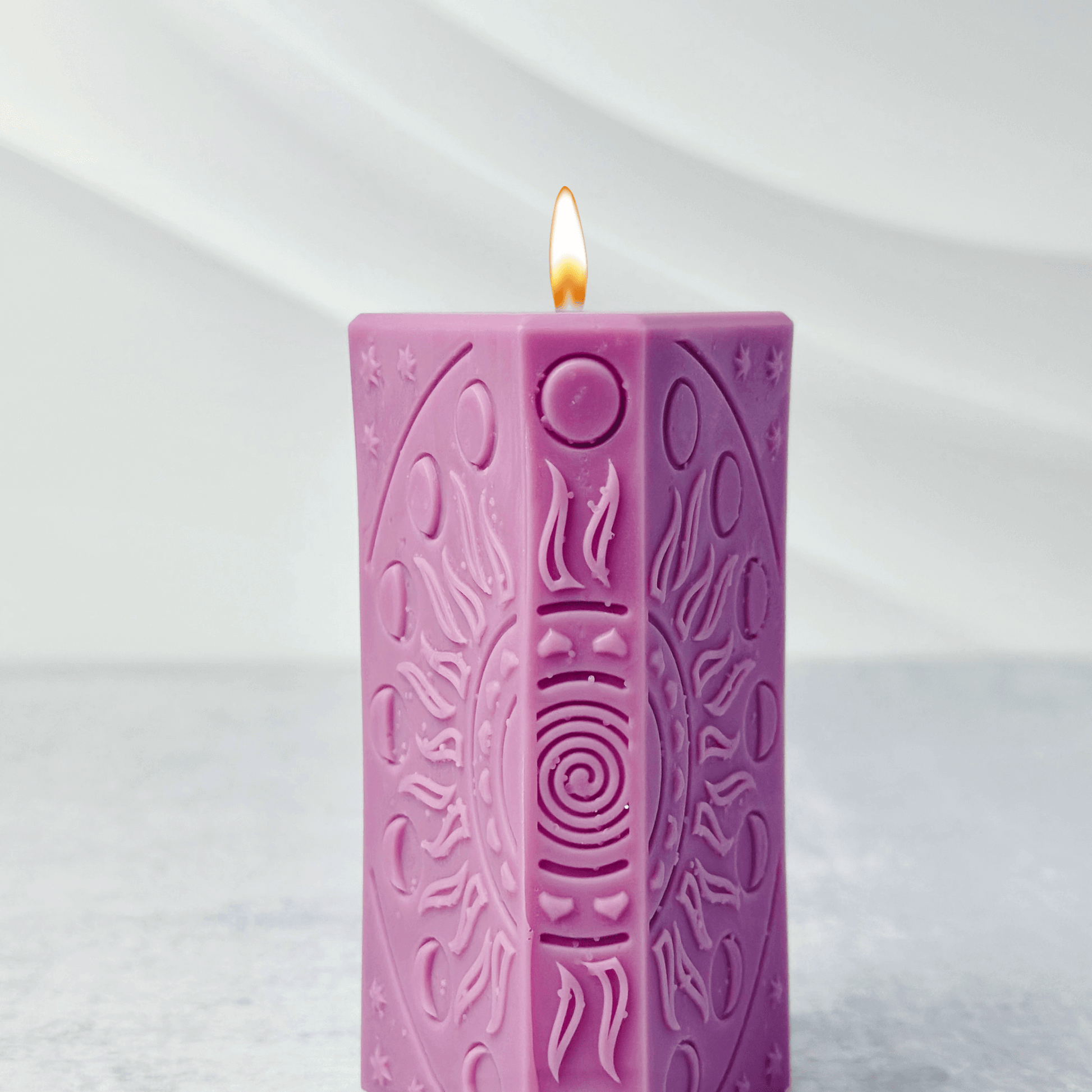 Pink candle with swirling designs and flame, showcasing a decorative mold for spiritual candle crafting.