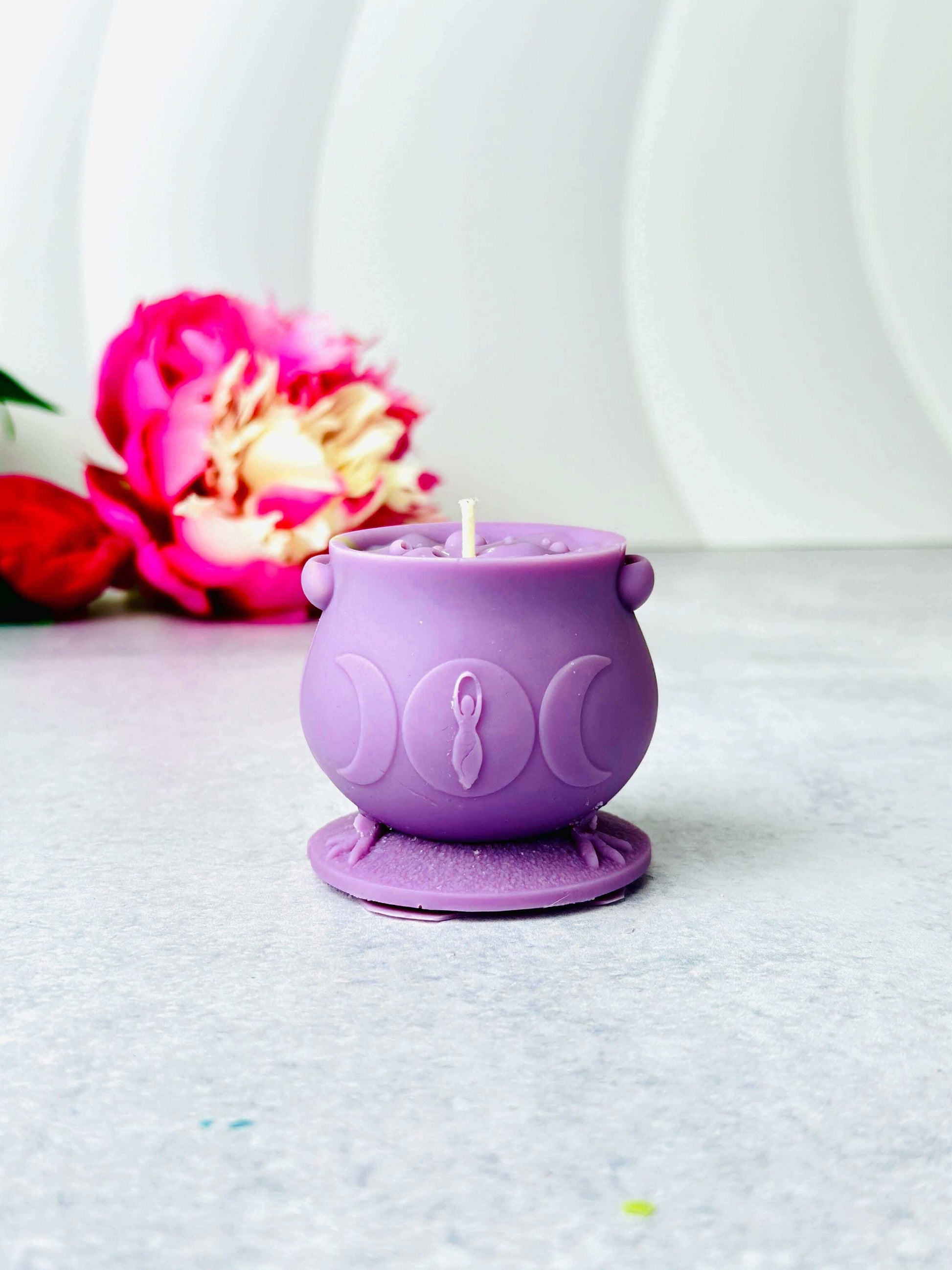 Purple witchcraft cauldron candle in a silicone mold, decorated with moon phases and placed on a light background.