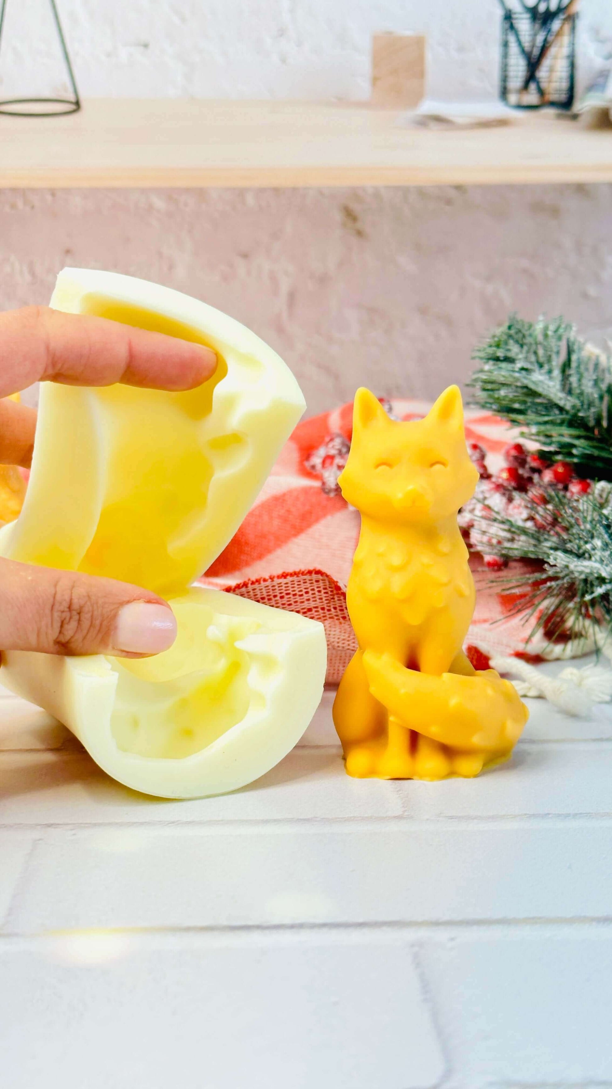Hand holding a fox-shaped silicone mold with a yellow candle beside it, showcasing DIY candle-making creativity.