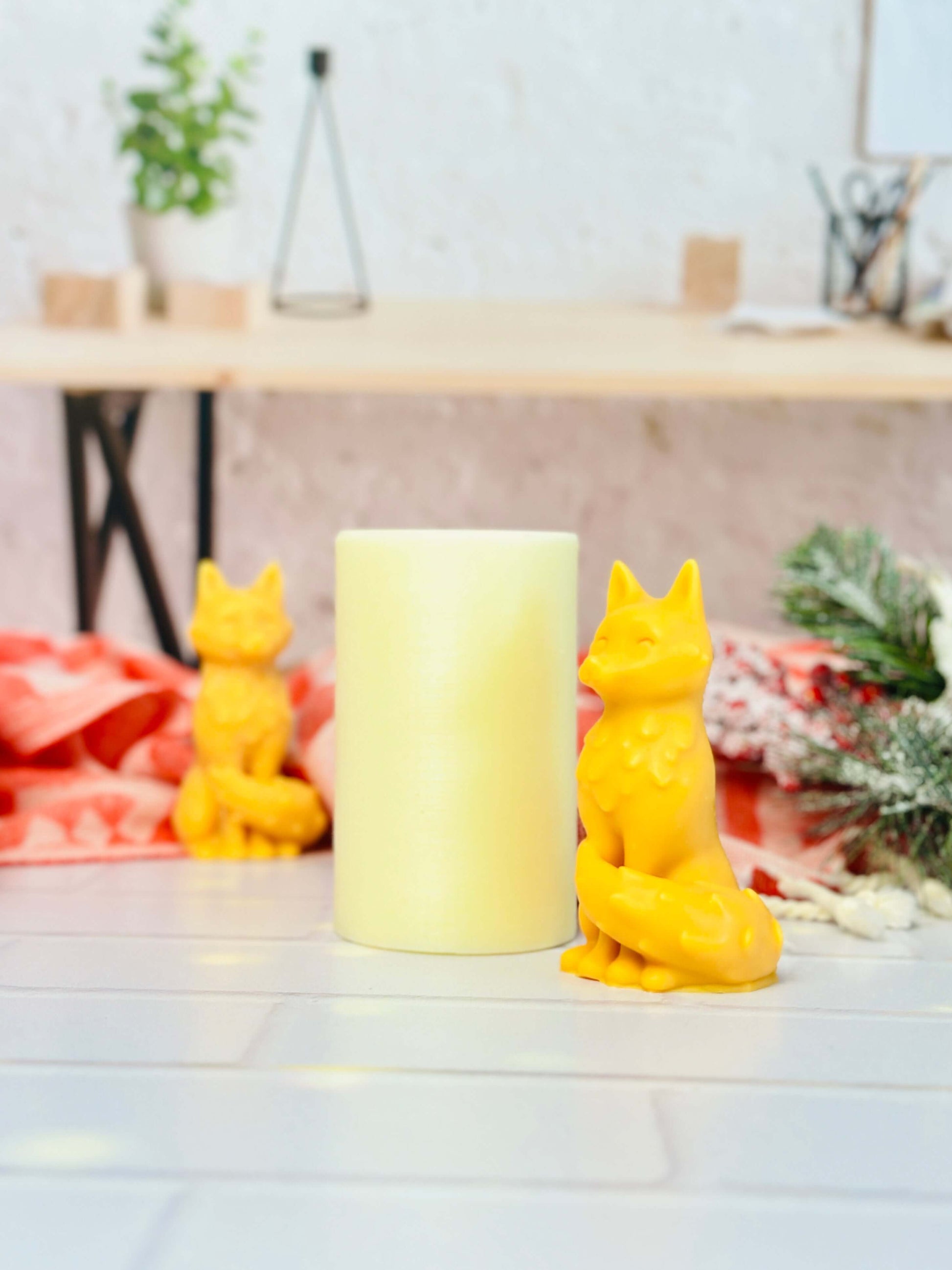 Yellow fox-shaped candle beside a pastel candle, surrounded by decorative elements on a wooden table.