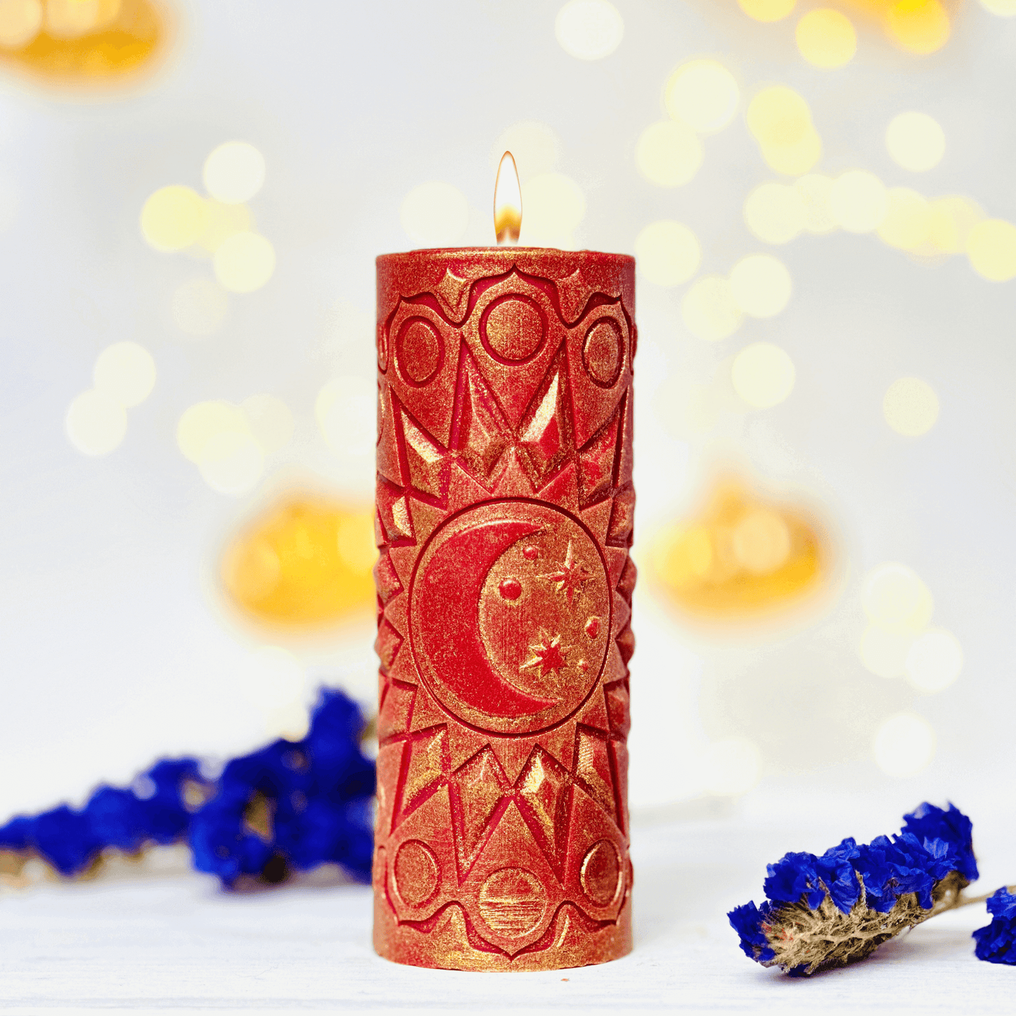 Red spiritual candle with moon and star patterns, surrounded by blue flowers and soft bokeh lighting.