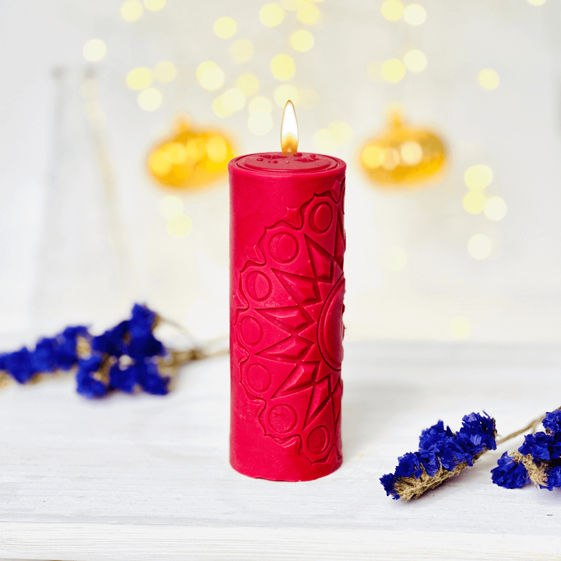 Red spiritual candle with sun pattern, surrounded by dried flowers and warm lights, creating a cozy atmosphere.