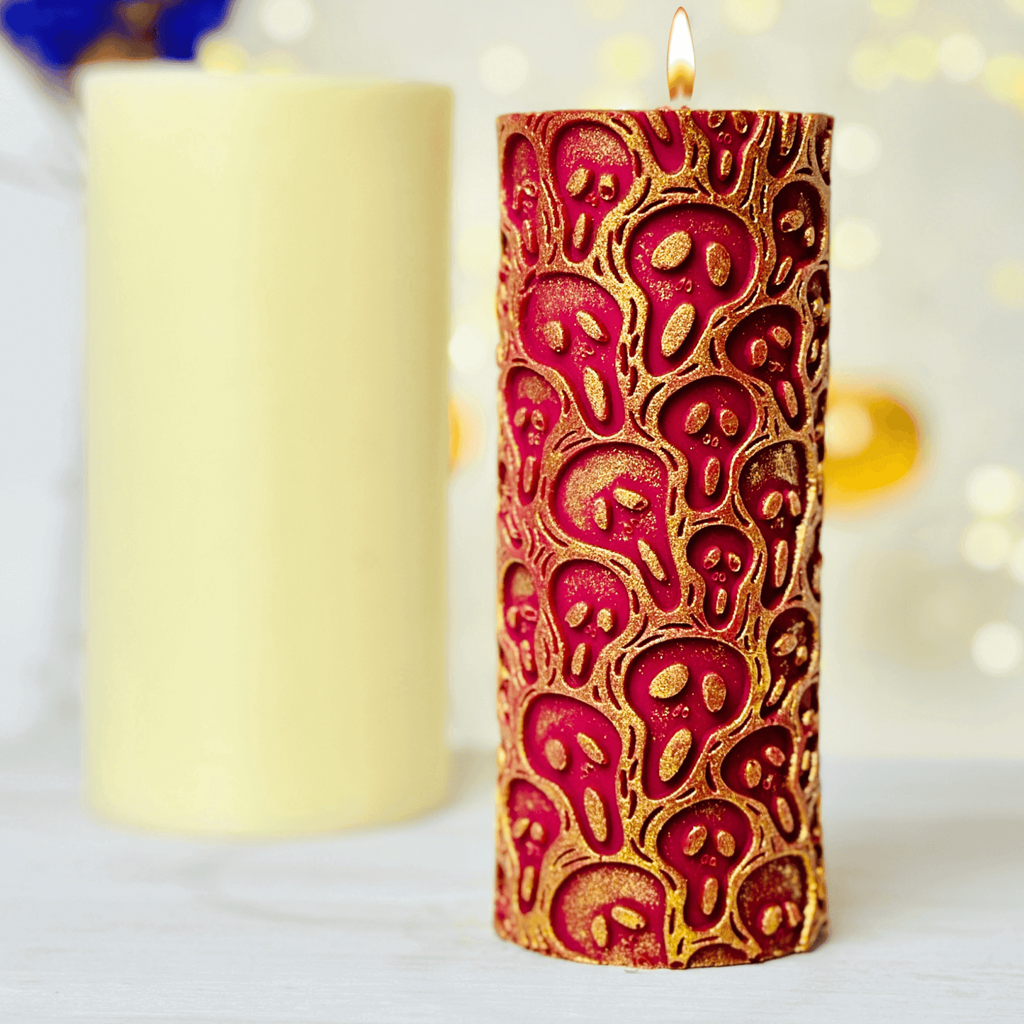 Spooky ghost design candle with red and gold accents for Halloween, next to a plain yellow candle.