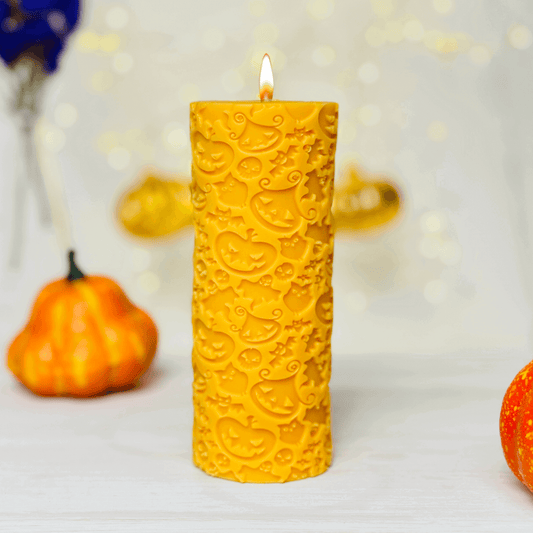 Yellow Halloween pillar candle with Bat and pumpkin designs, surrounded by seasonal decor.