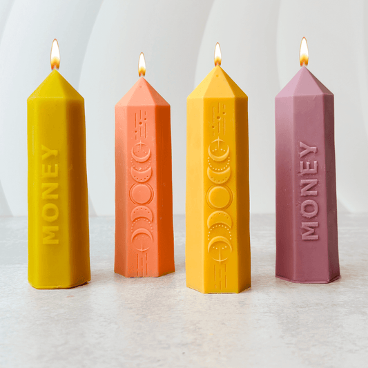 Four colorful candles in various shapes and sizes, labeled for money attraction, inspired by moon phases.